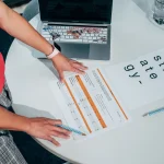 Hands organizing CRM proposal documents and evaluation criteria on a conference table