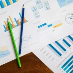 Analyst reviewing downward-trending economic charts and financial data on desk with documents and globe