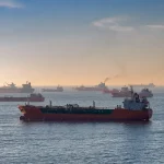 Cargo ship navigating a strategic maritime strait with oil tankers in the distance