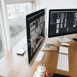 Insurance agent working at desk with multiple computer screens displaying CRM software and customer data