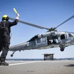 Military helicopter conducting naval operation over disabled container ship in Gulf of Oman