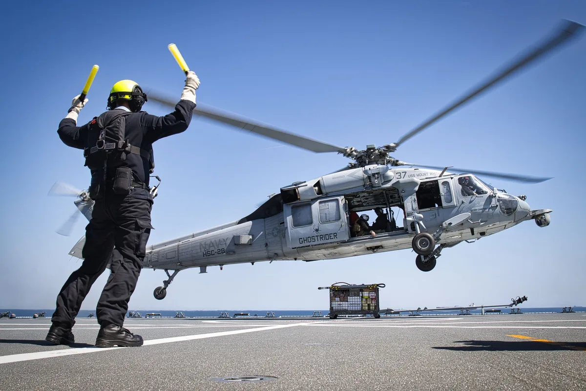 Military helicopter conducting naval operation over disabled container ship in Gulf of Oman