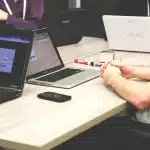 Hands at a laptop with printed keyword lists and an analytics printout on a desk
