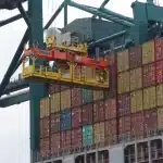 Deck of a cargo ship with unbranded crates and workers near a lighthouse under cold light