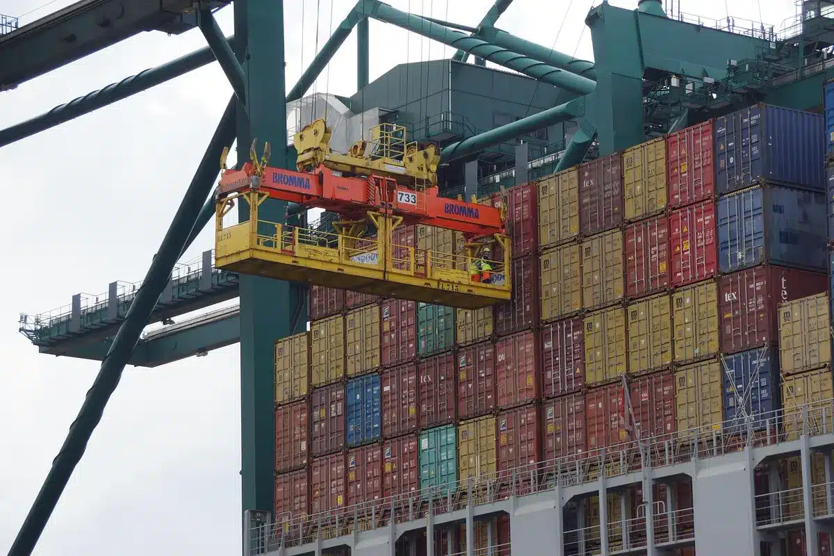 Deck of a cargo ship with unbranded crates and workers near a lighthouse under cold light
