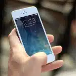 Hands typing on a laptop with notepad and smartphone, blurred charts on screen